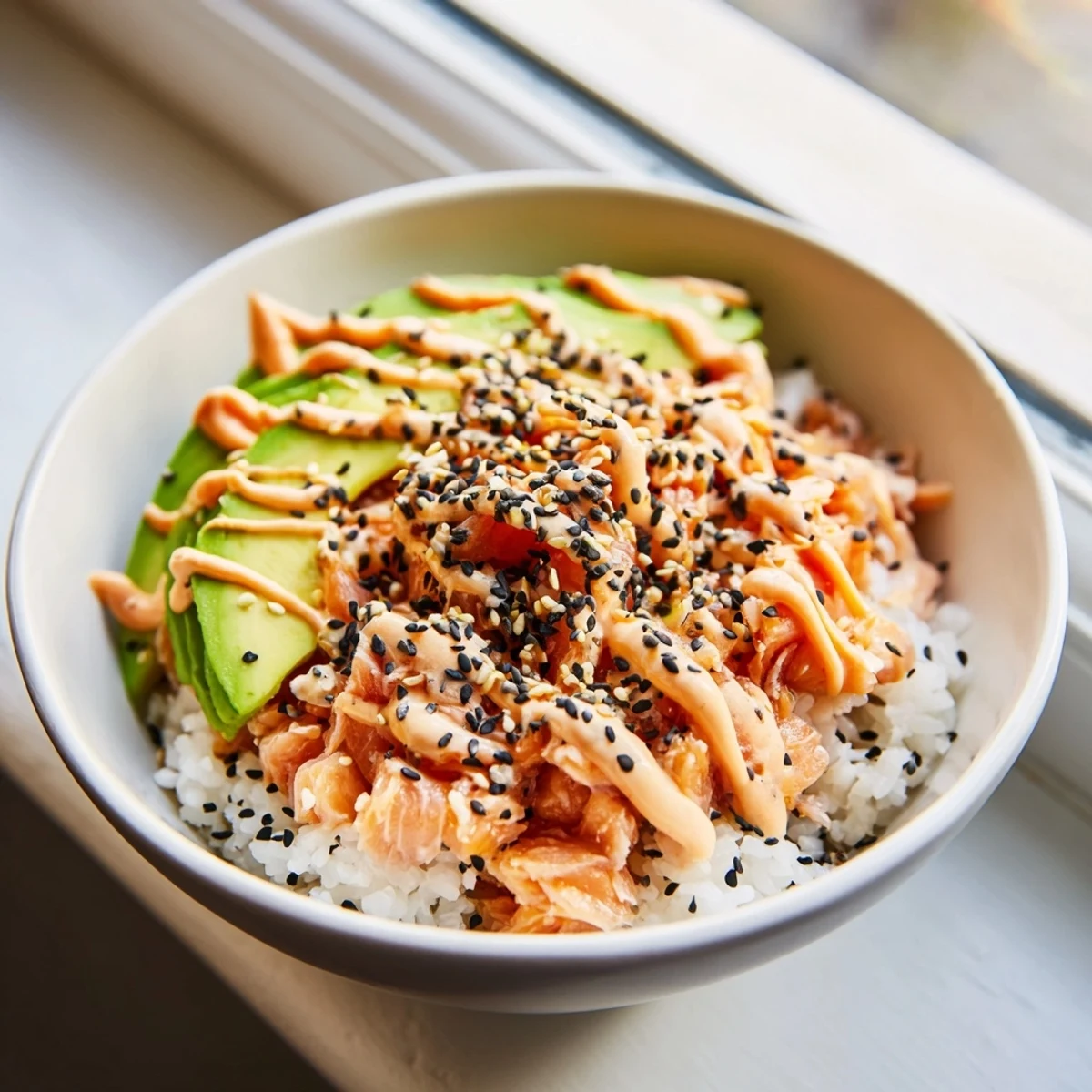A vibrant Japanese-American salmon rice bowl featuring tender salmon, seasoned rice, and avocado with a drizzle of spicy mayo.
