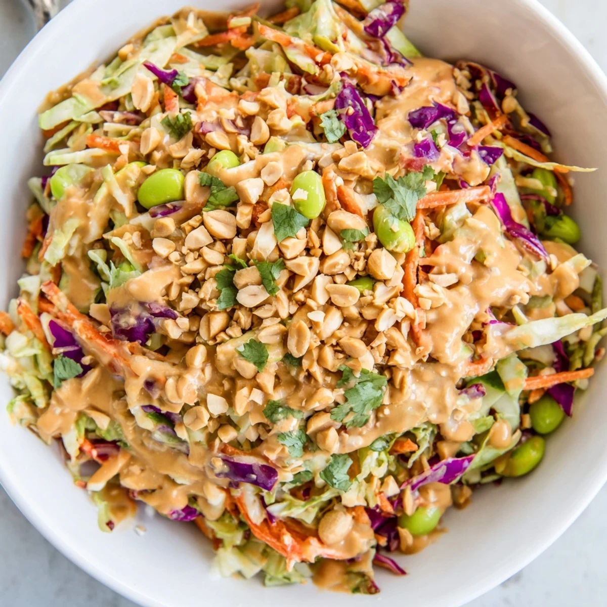 Shredded cabbage, carrots, and edamame are tossed in a creamy peanut dressing for this vibrant, crunchy Thai Peanut Salad, served with lime wedges and peanuts.