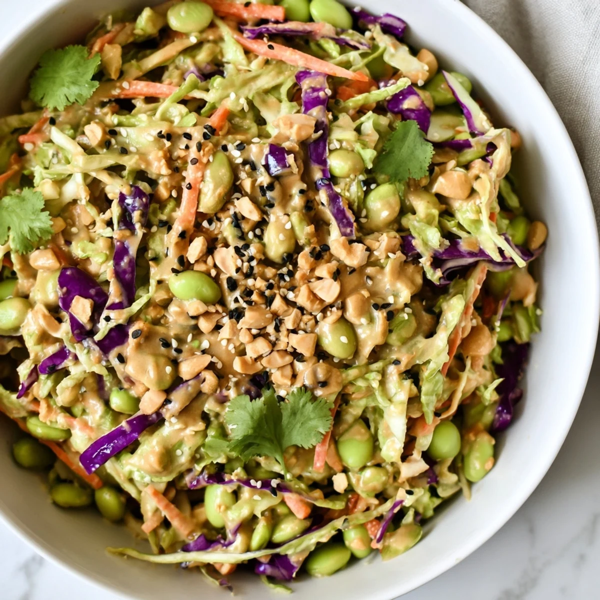 A bowl of Thai Peanut Salad showcases fresh cilantro, crisp bell peppers, and edamame coated in a savory, tangy peanut dressing.