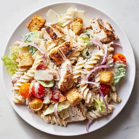 This image shows a vibrant bowl of Chicken Caesar Pasta Salad, garnished with fresh Parmesan and croutons.