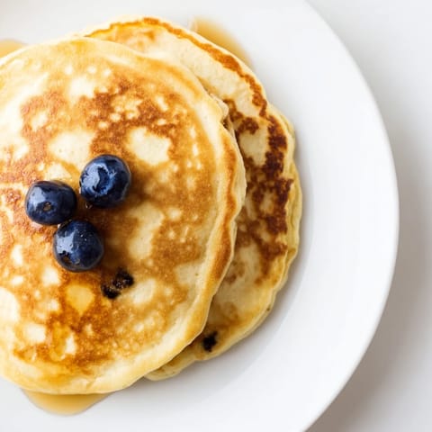 Freshly cooked cottage cheese pancakes steam gently on a griddle, their fluffy edges golden, ready to be served with a dollop of Greek yogurt.