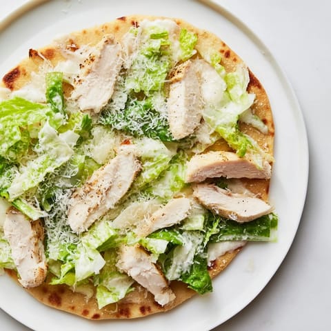 A close-up of a savory Chicken Caesar Flatbread topped with juicy sliced chicken, chopped lettuce, parmesan, and optional cherry tomatoes.  