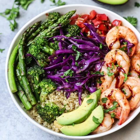Freshly prepared Detox Buddha Bowl with Shrimp and Quinoa topped with colorful cabbage, diced tomatoes, and a balsamic olive oil drizzle.