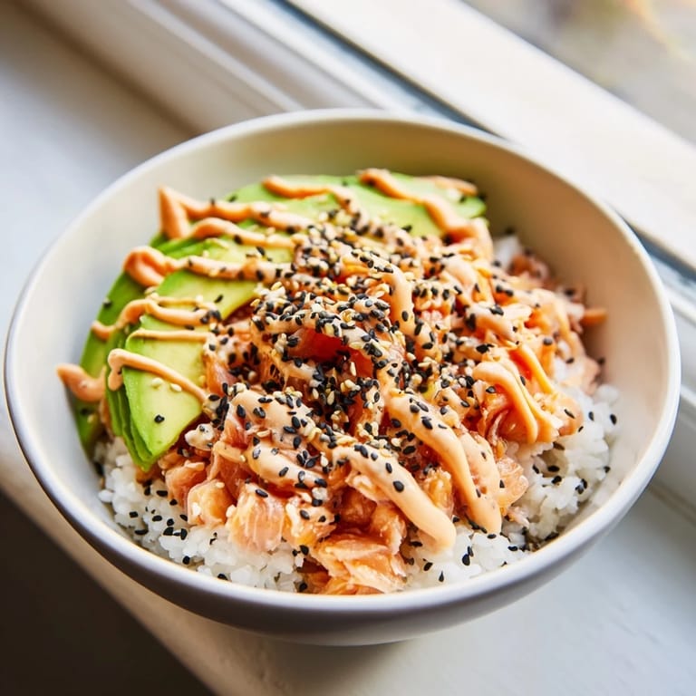 A vibrant Japanese-American salmon rice bowl featuring tender salmon, seasoned rice, and avocado with a drizzle of spicy mayo.