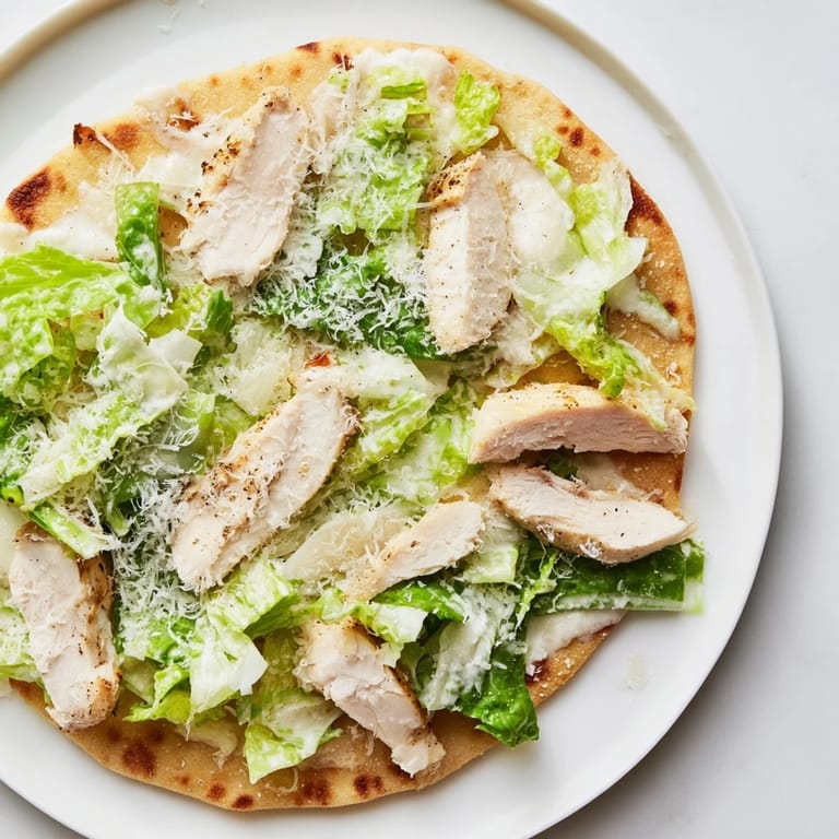 A close-up of a savory Chicken Caesar Flatbread topped with juicy sliced chicken, chopped lettuce, parmesan, and optional cherry tomatoes.  